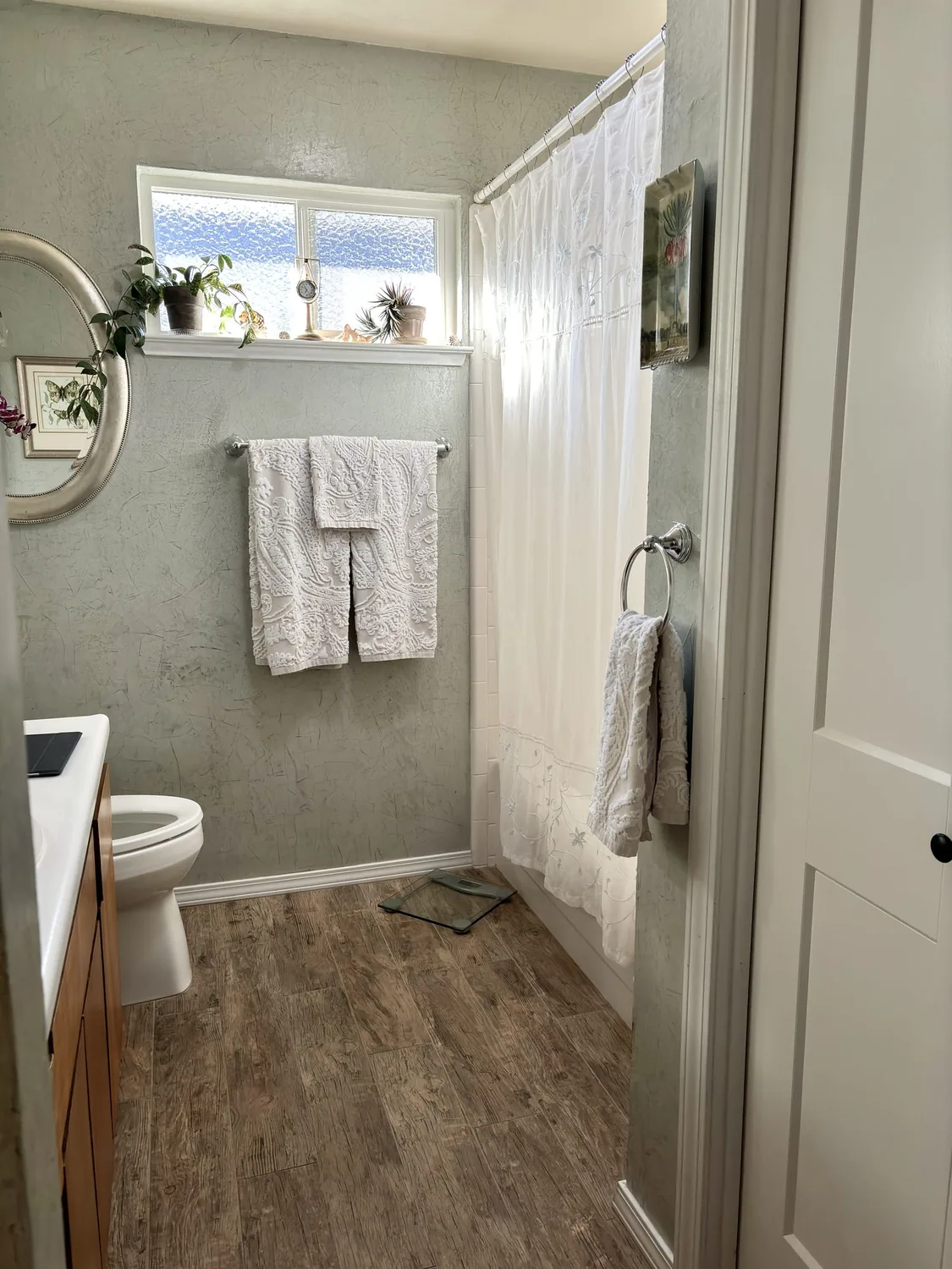 A bathroom corner with a white bathtub, wooden slat wall paneling, two framed paintings, a small wooden stool