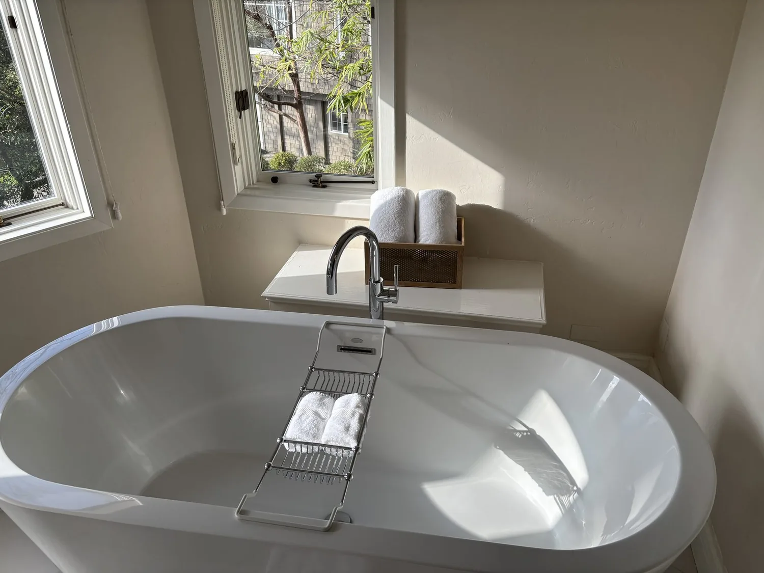 A bright bathroom with a white freestanding bathtub, chrome faucet, and rolled white towels near a window