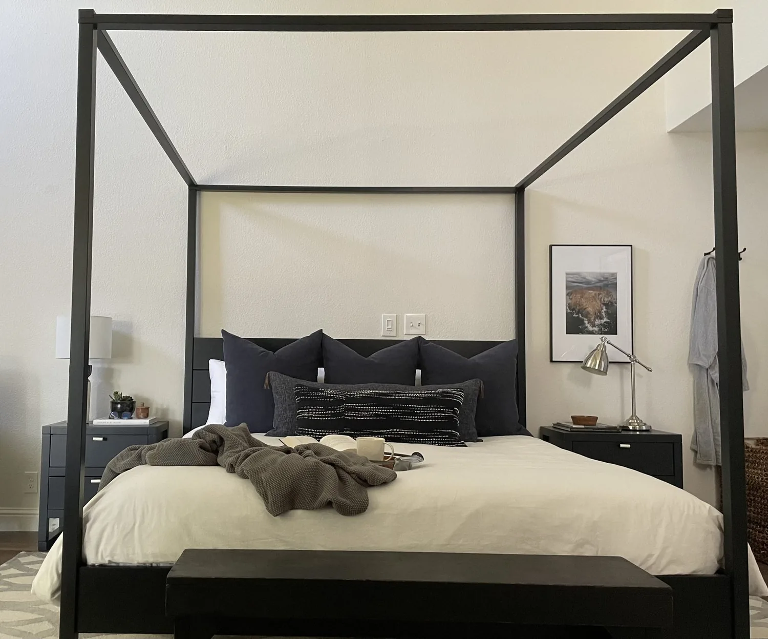 A minimalist bedroom with a beige upholstered bed, white bedding, two framed abstract artworks, floating wooden