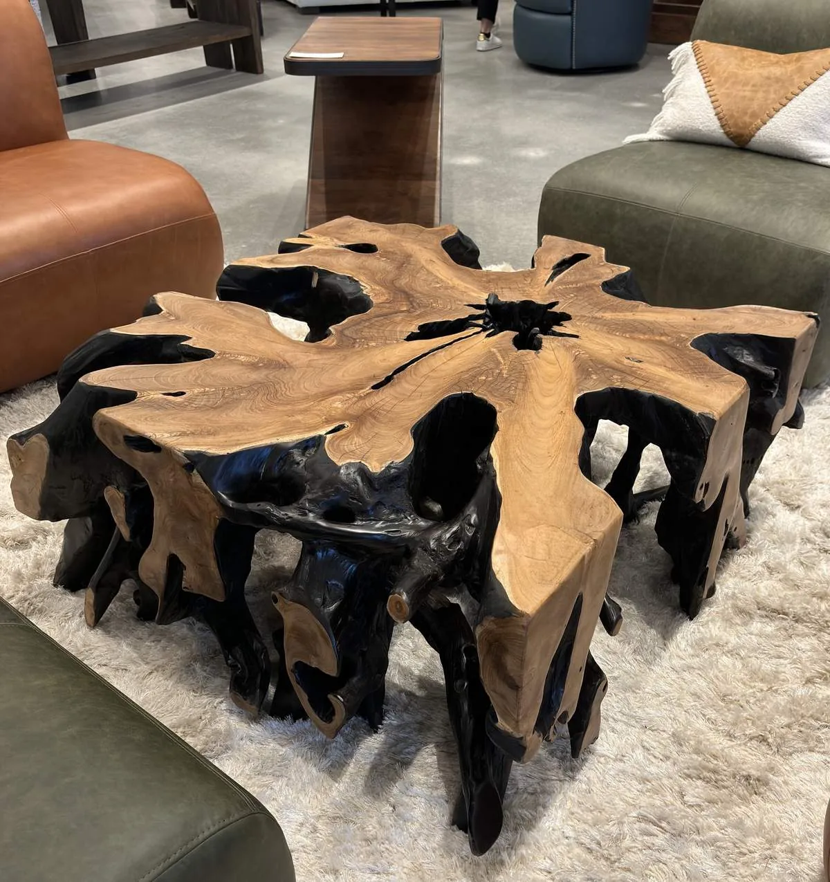 A unique wooden coffee table with a natural, irregular shape surrounded by leather and fabric seating on a plush rug