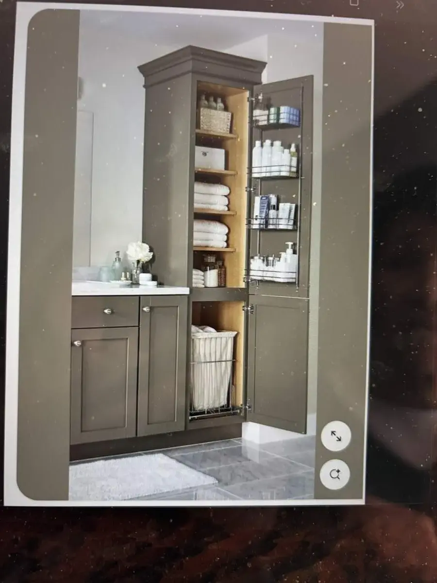 A bathroom cabinet with open doors showing organized shelves with towels, bottles, and a laundry basket