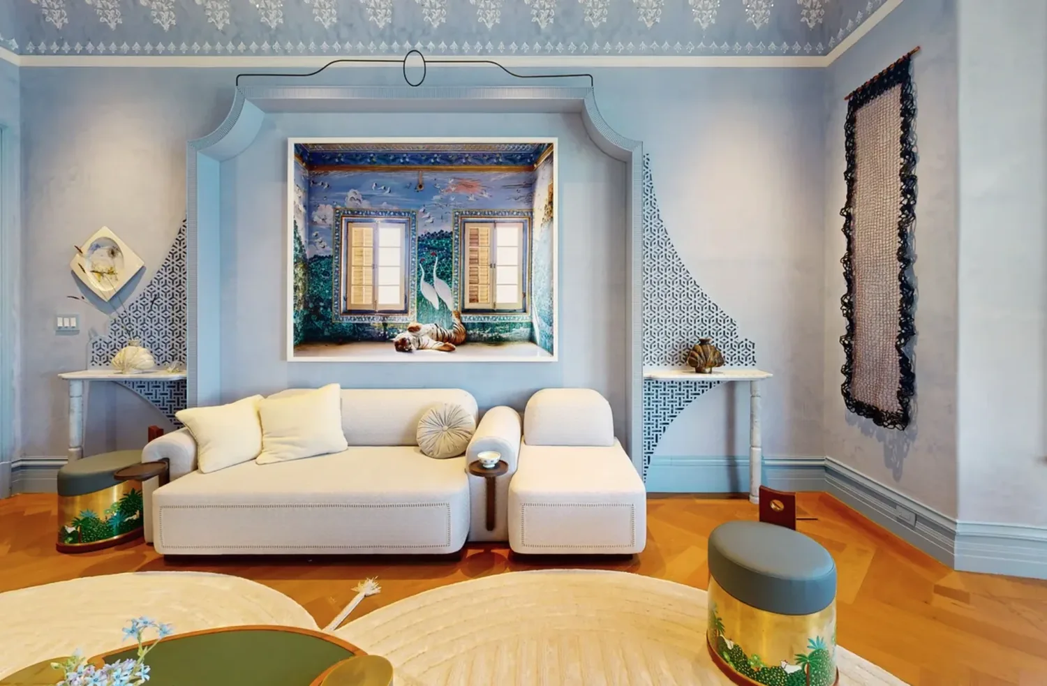 A stylish living room with a cream sofa, blue walls featuring intricate patterns, and a large framed artwork of a tiger in a decorated room