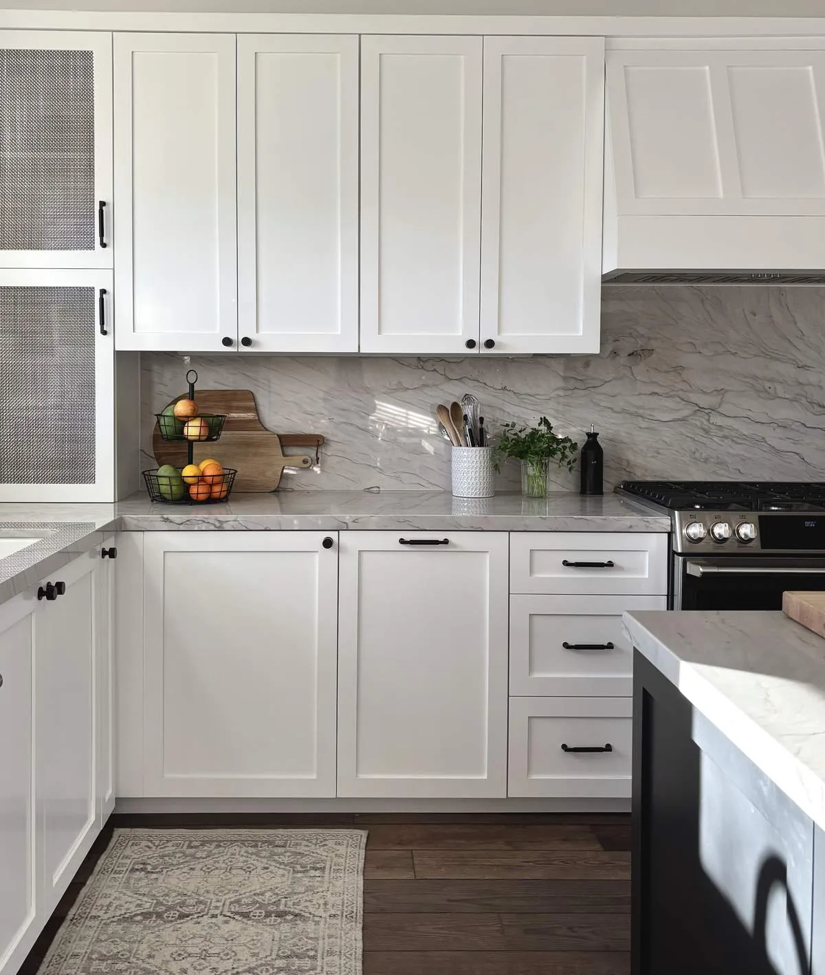 A modern kitchen with white cabinetry, marble countertops and backsplash, a gas stove, and wooden flooring