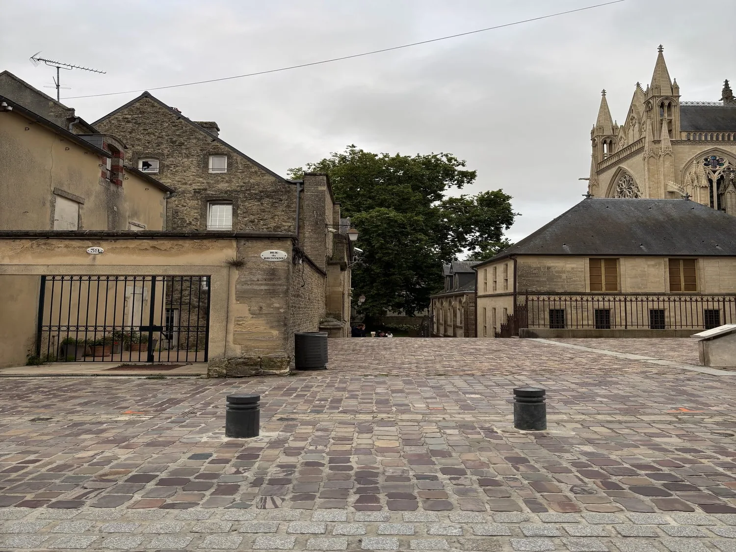 A cobblestone street with historic stone buildings and a Gothic-style church in the background under a cloudy sky