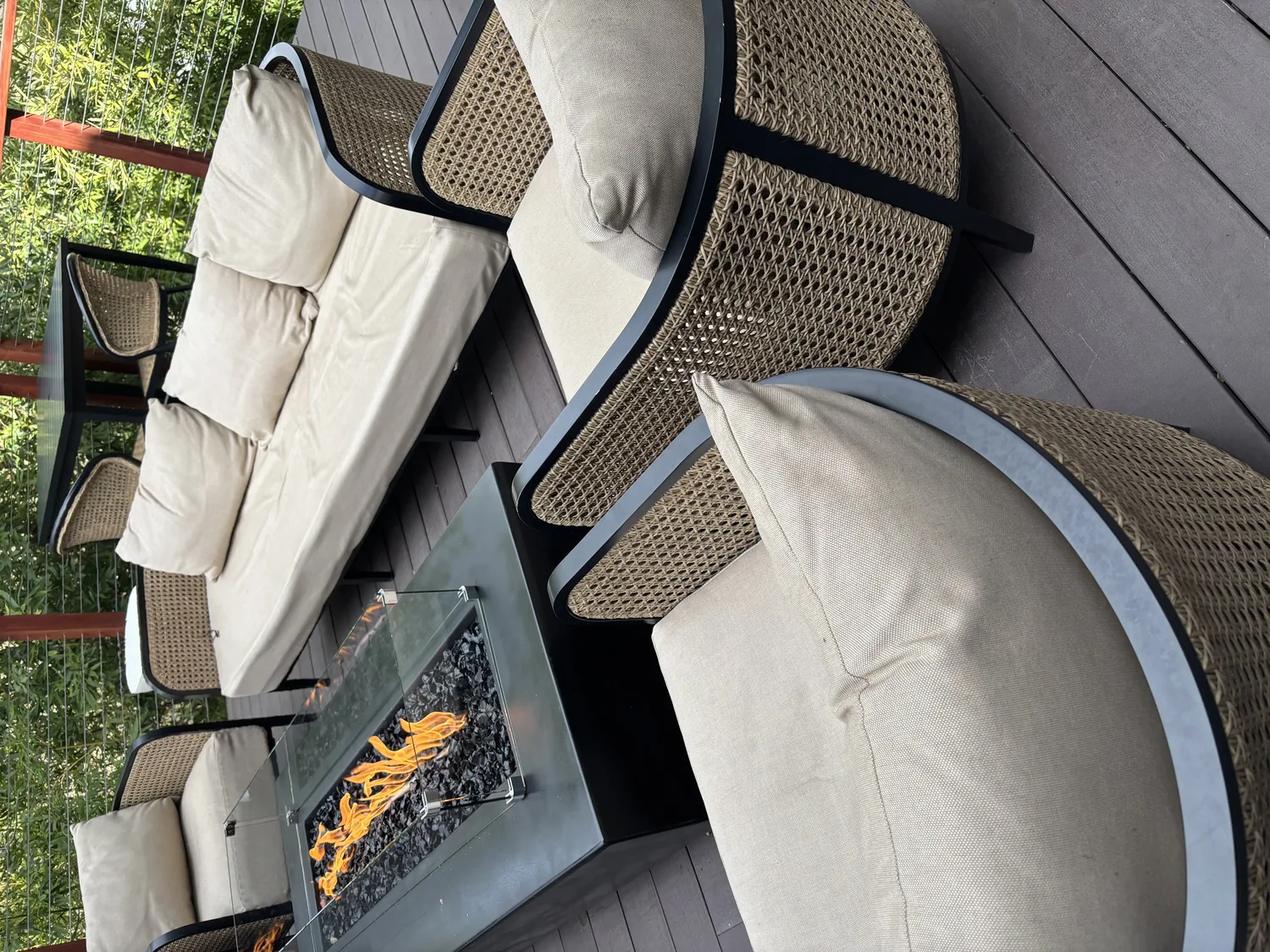 Outdoor seating area with beige cushioned wicker chairs and a fire pit table on a wooden deck