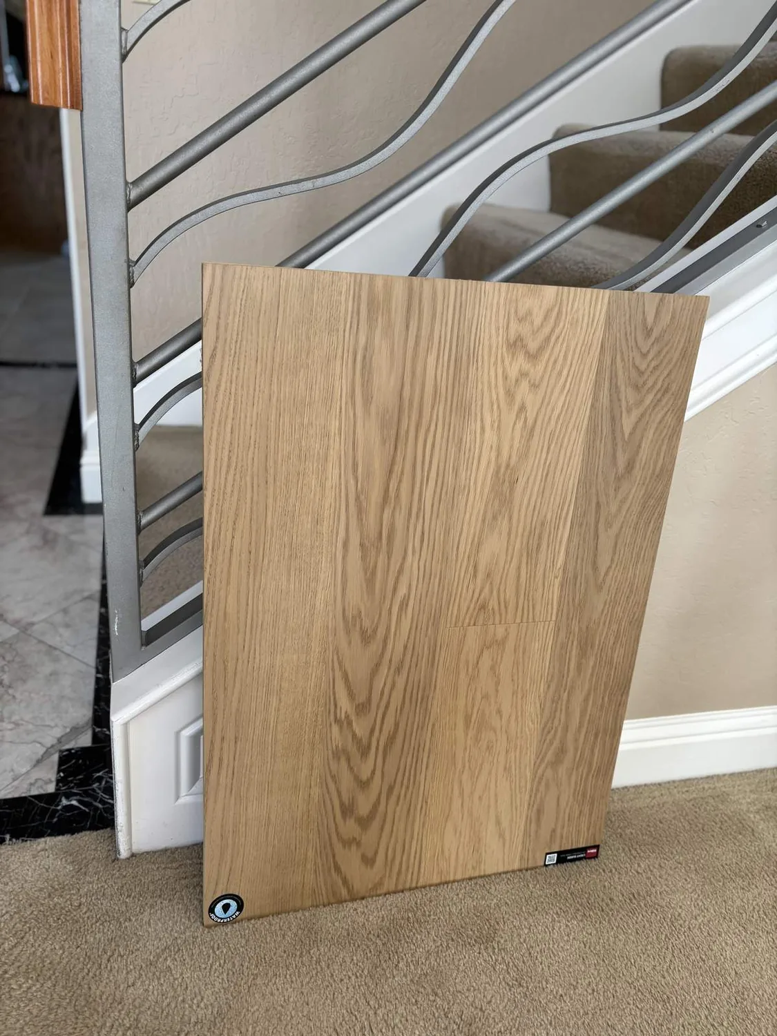 A sample of light wood flooring leaning against a metal stair railing inside a home