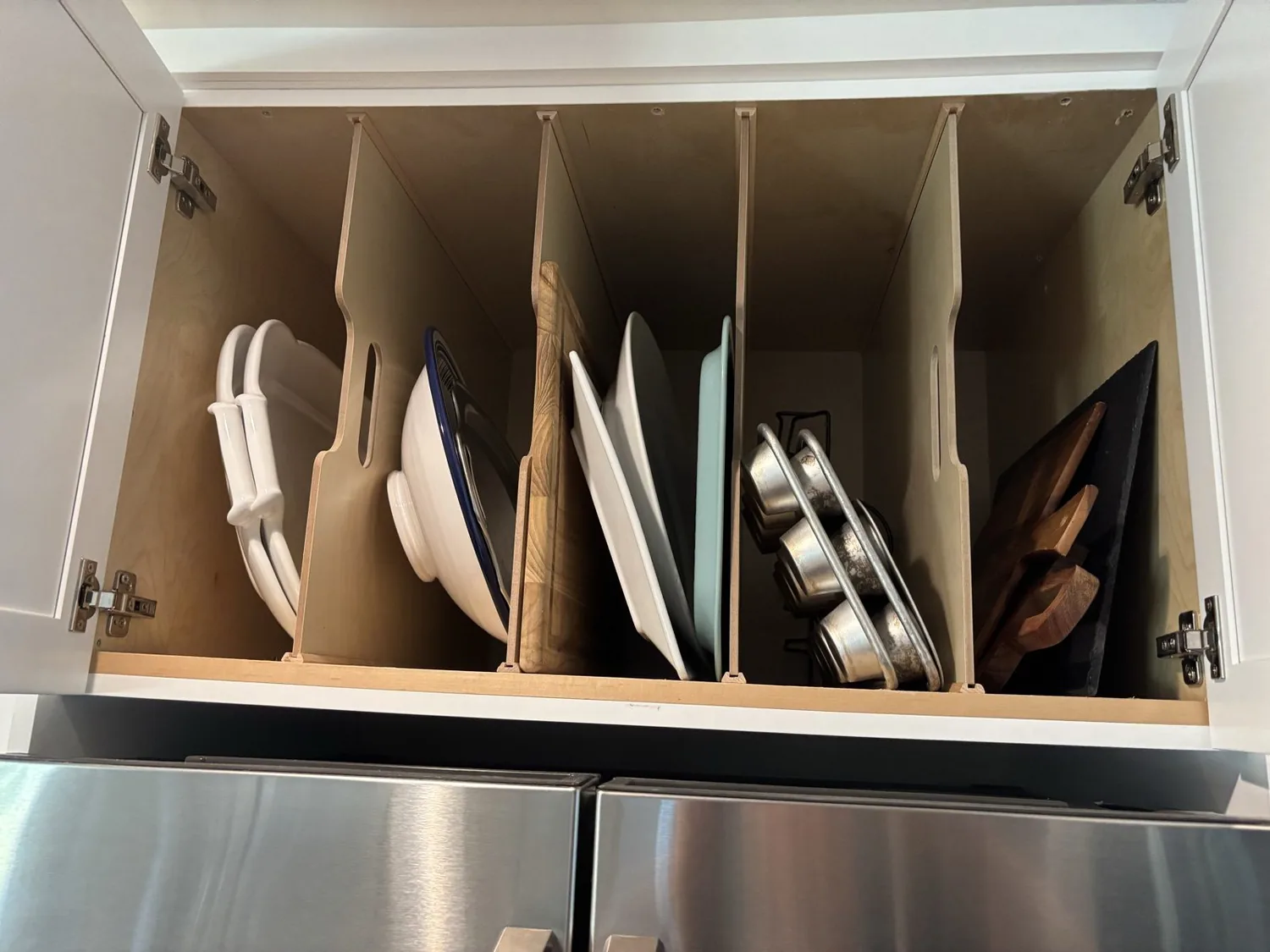 An organized kitchen cabinet with vertical dividers storing plates, cutting boards, and baking pans