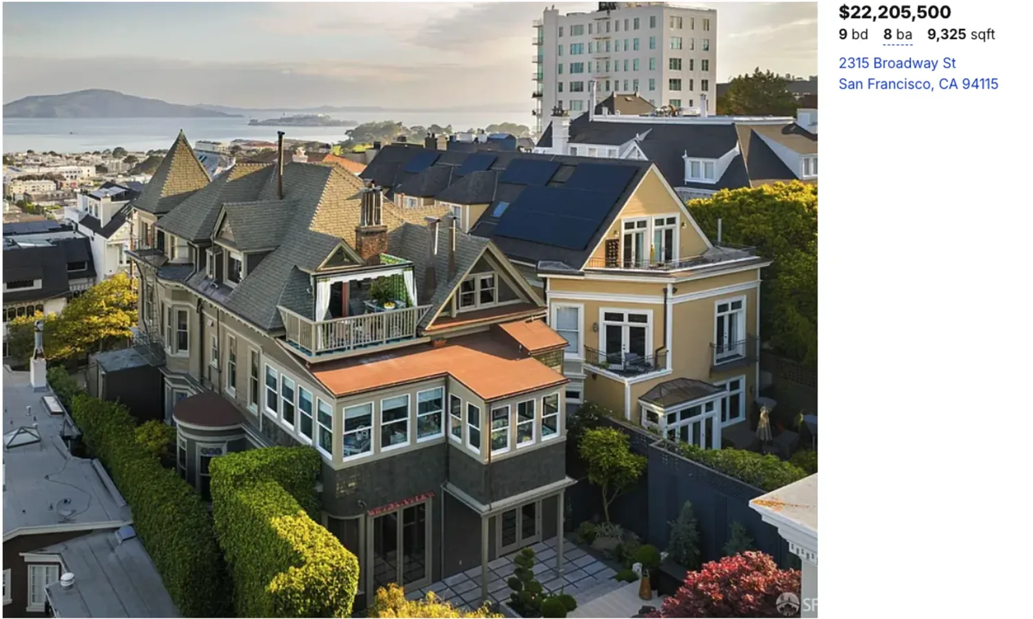 A large, multi-story Victorian-style house with a garden and cityscape in the background