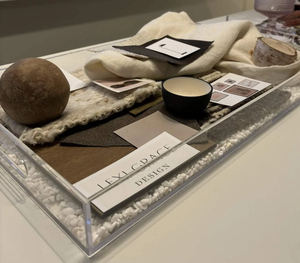 A clear tray containing fabric swatches, a small bowl, a wooden sphere, a piece of birch wood, and design sample cards
