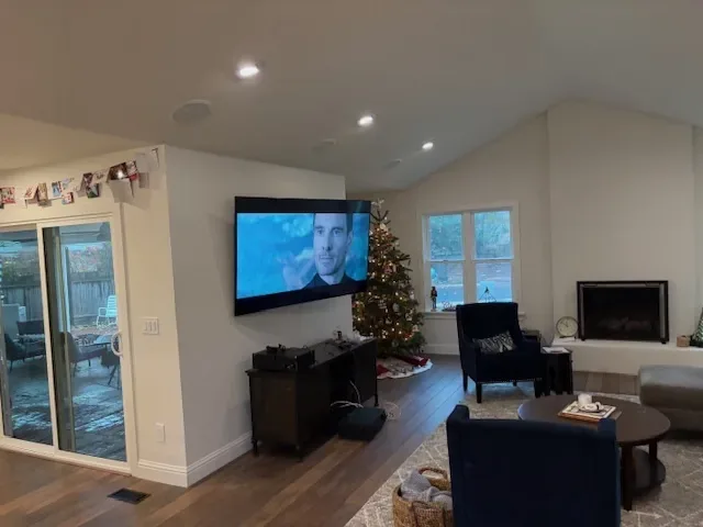 A modern living room with a wall-mounted TV, Christmas tree, dark blue chairs, a fireplace, and sliding glass doors leading outside